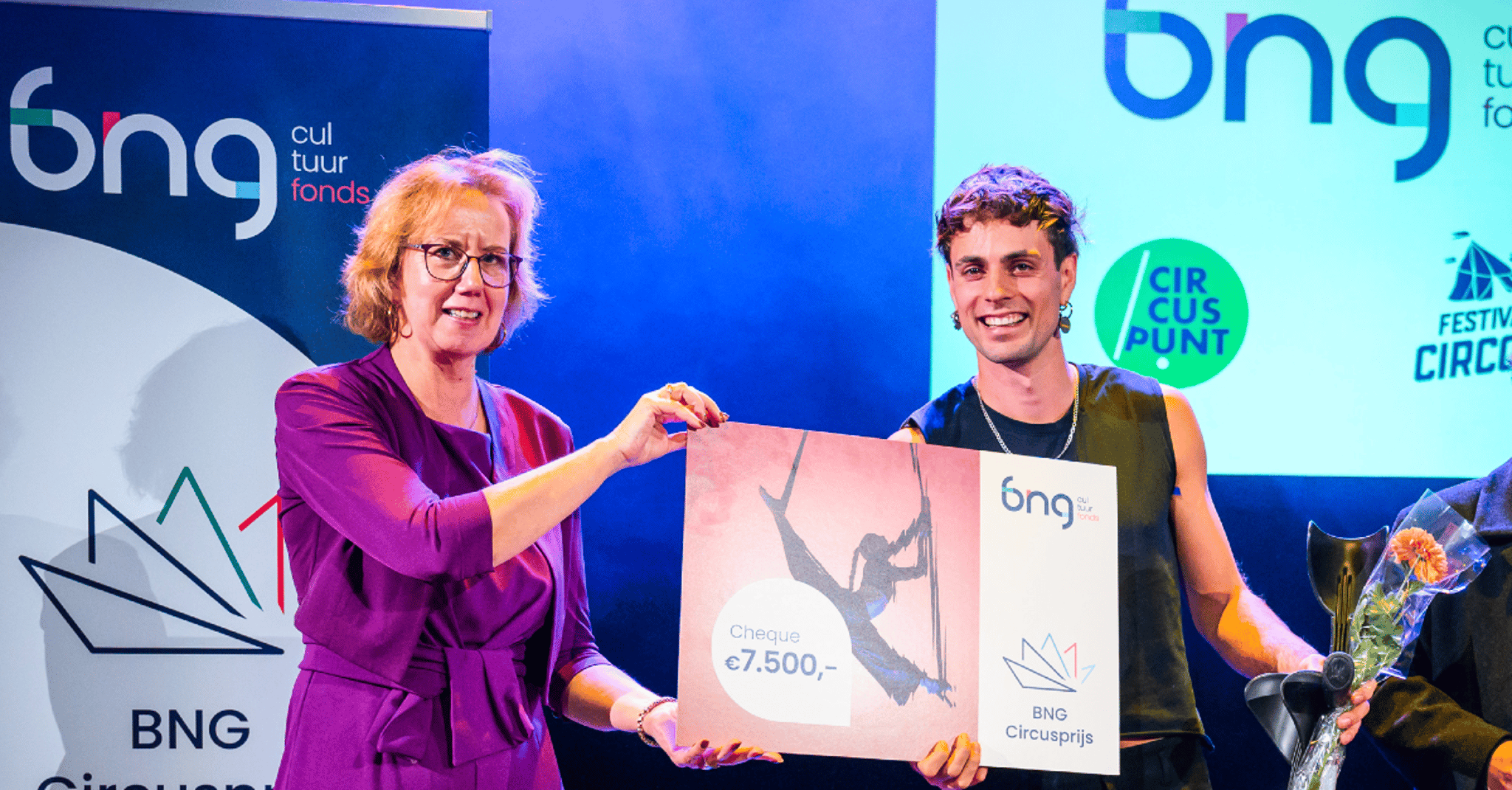 Margo Mulder, Burgemeester van Bergen op Zoom en bestuurslid van het BNG Cultuurfonds, reikt Tim van den Bos de Lucas de Circusprijs 2025 uit op het podium.