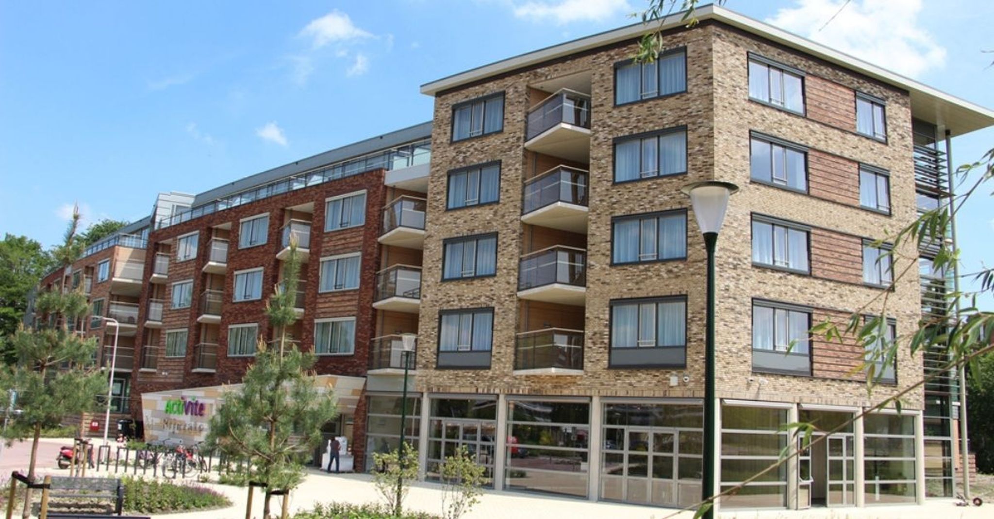 Een nieuw verpleeghuis met zorgappartementen met een rode en een zandkleurige gevel met balkons.