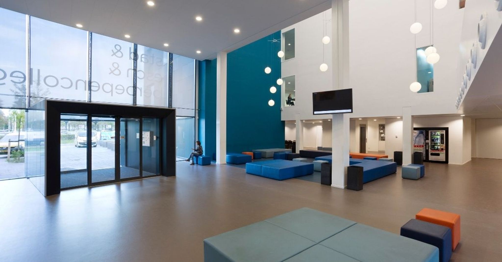 Entree van Onderwijspark Ezinge met hoog wit plafond, een blauwe en witte muur, en blauwe blokken om op te zitten.