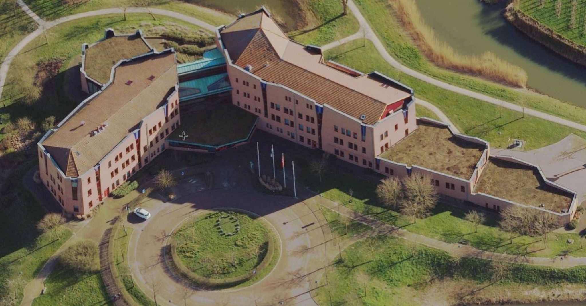 Een gebouw van boven bekeken met meerdere verdiepingen, een grote entree en veel gras eromheen.