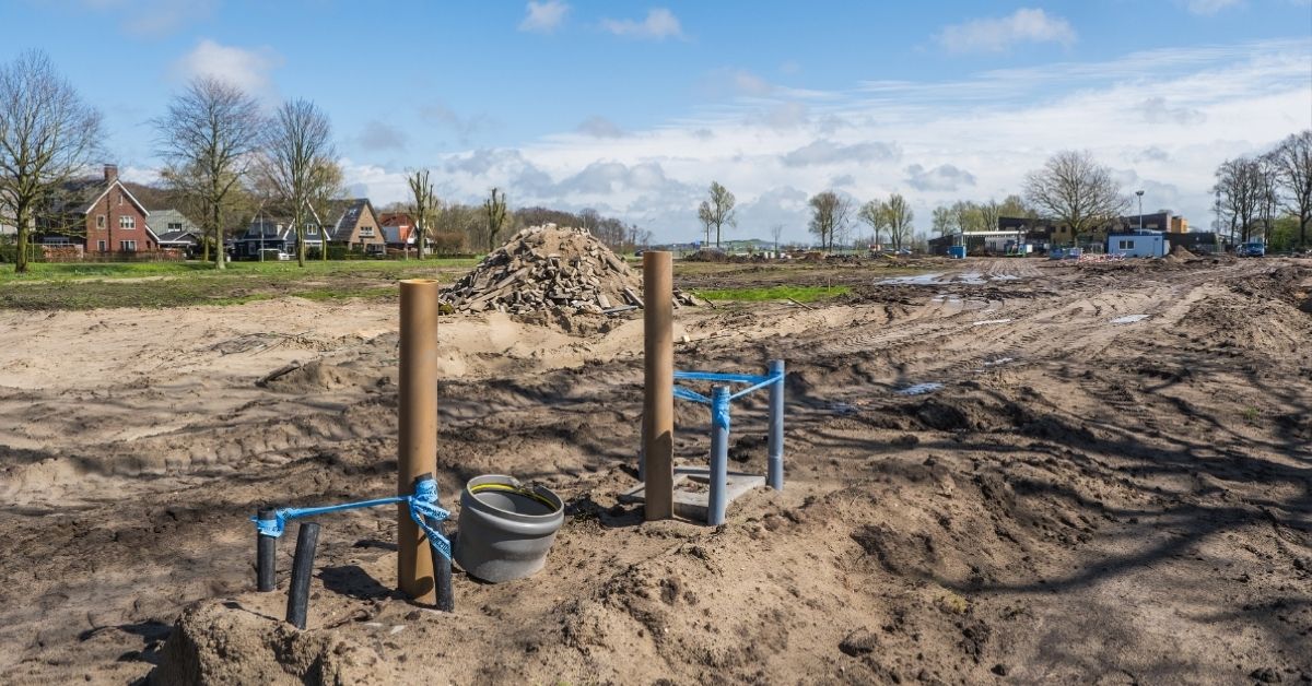Een grasveld dat verandert in een bouwplaats met modder, een stapel stenen en de eerst palen.