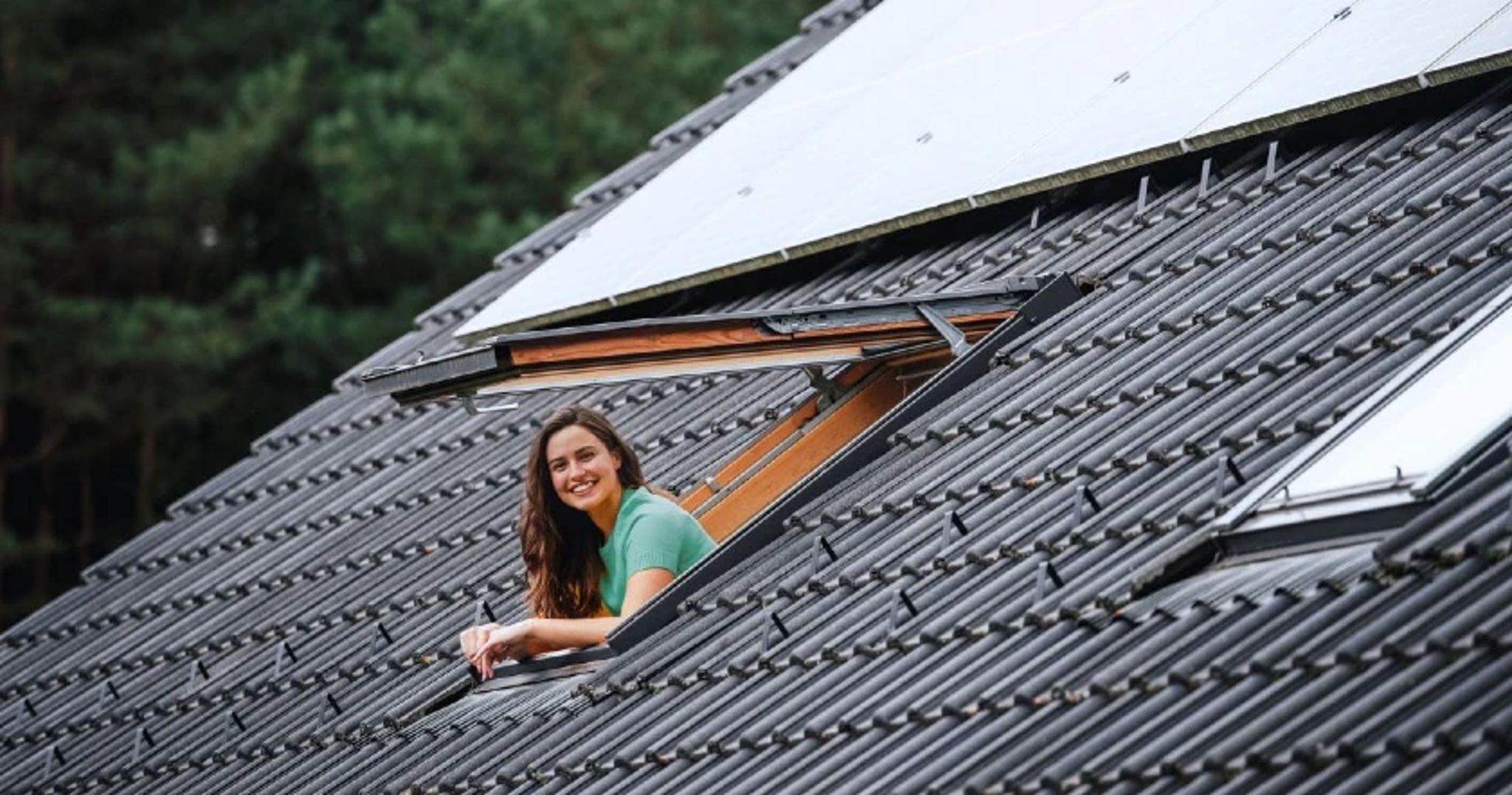 Schuin dak met zonnepanelen en dakraam waar een jonge vrouw uit hangt.