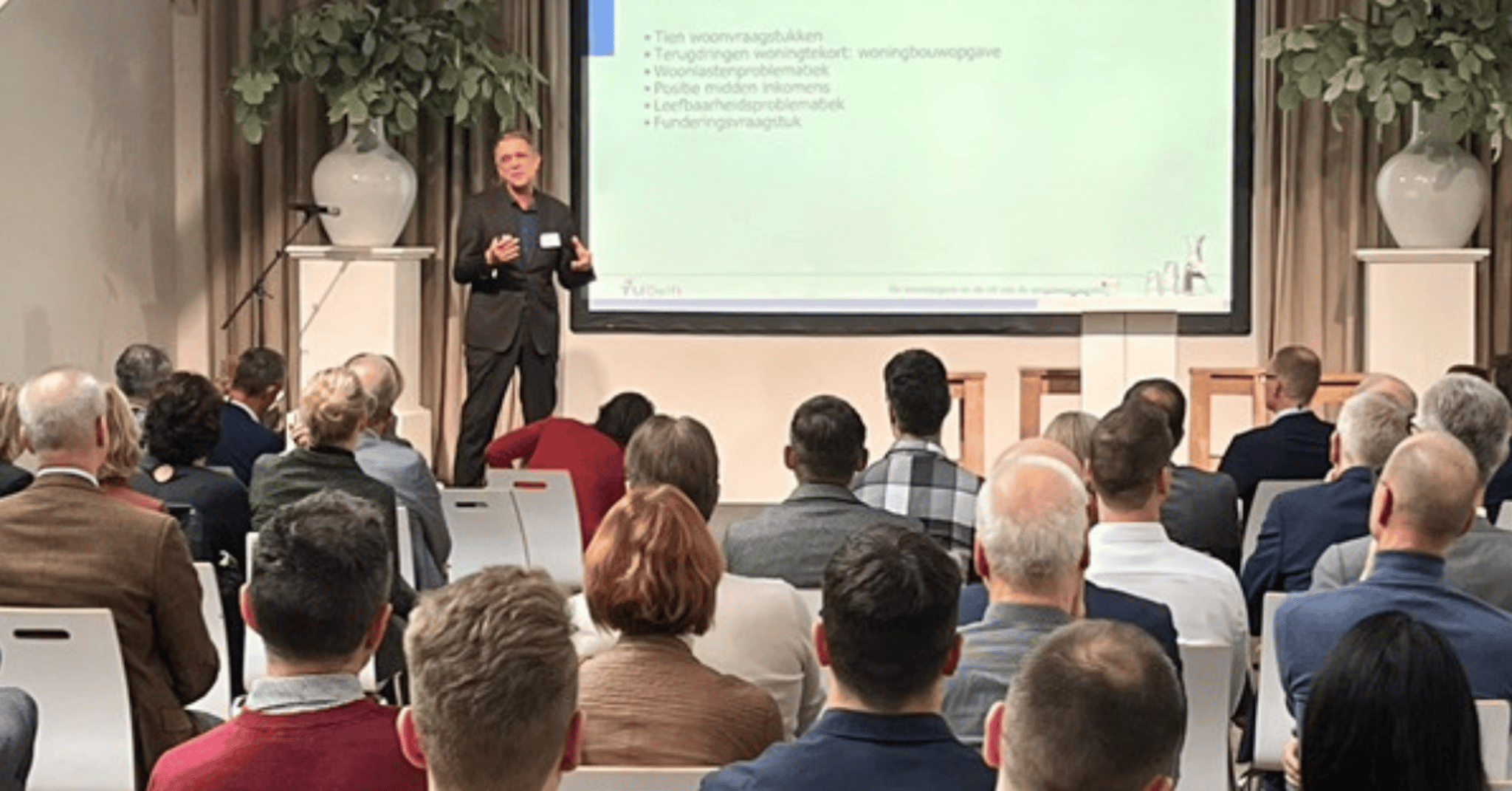 Persoon presenteert aan een zaal over het onderwerp woonvraagstukken.