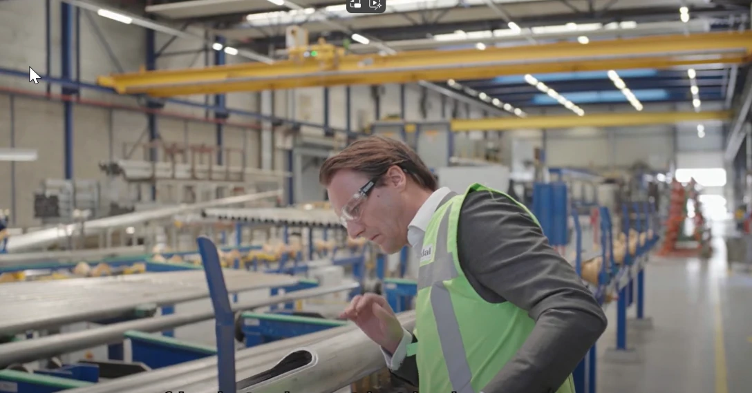 Man in fabriekshal met veiligheidsbril en groen hesje bekijkt een product.