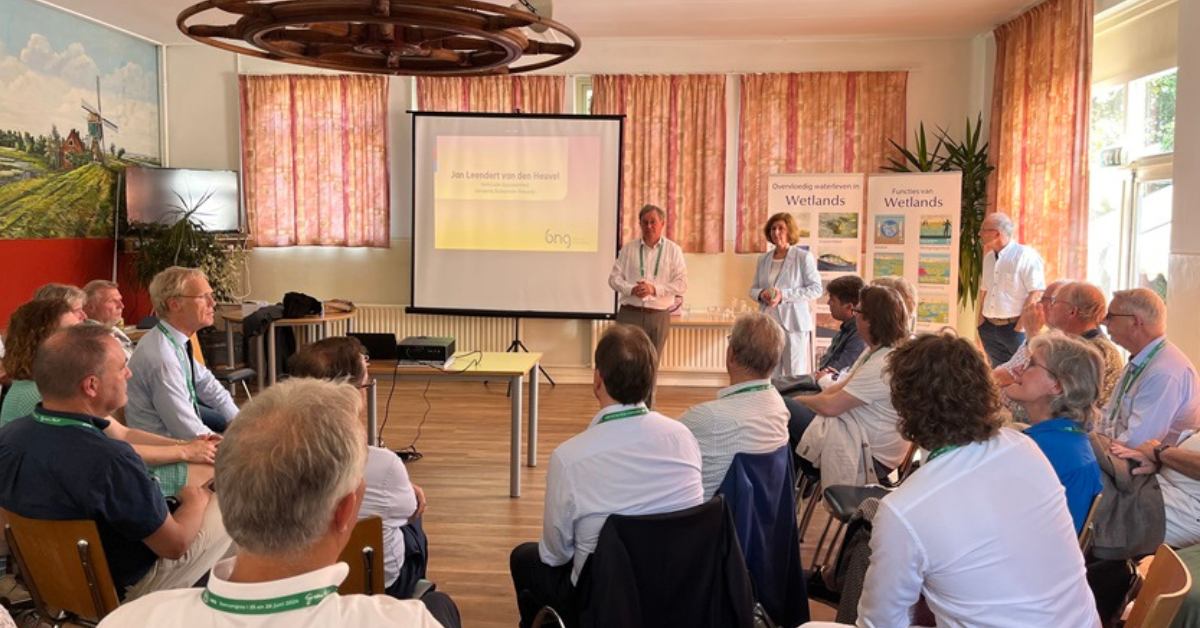 Twee mensen geven een presentatie in een kleine zaal. De aanwezigen zitten om hen heen.